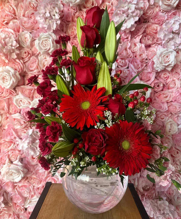 Red roses and gerbera daisies arranged in a clear glass vase