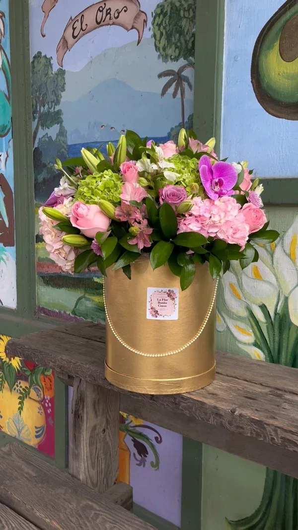 Pink and green floral arrangement in a gold hatbox