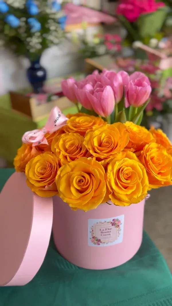 Pink tulips and orange roses in a pink hatbox with ribbon