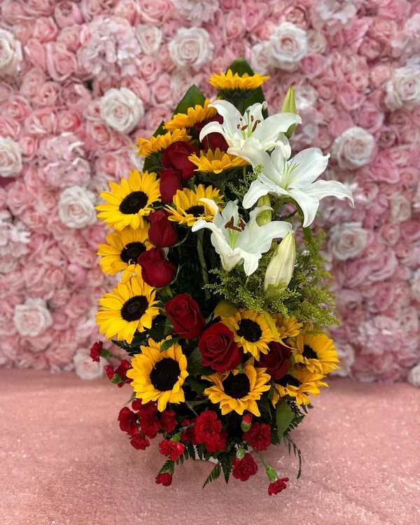 Bouquet of red roses, sunflowers, and white lilies against a pink rose wall