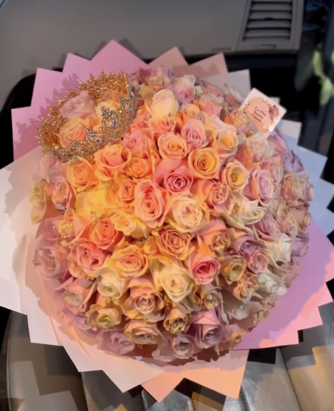 Large bouquet of pastel roses wrapped in pink paper with a decorative crown