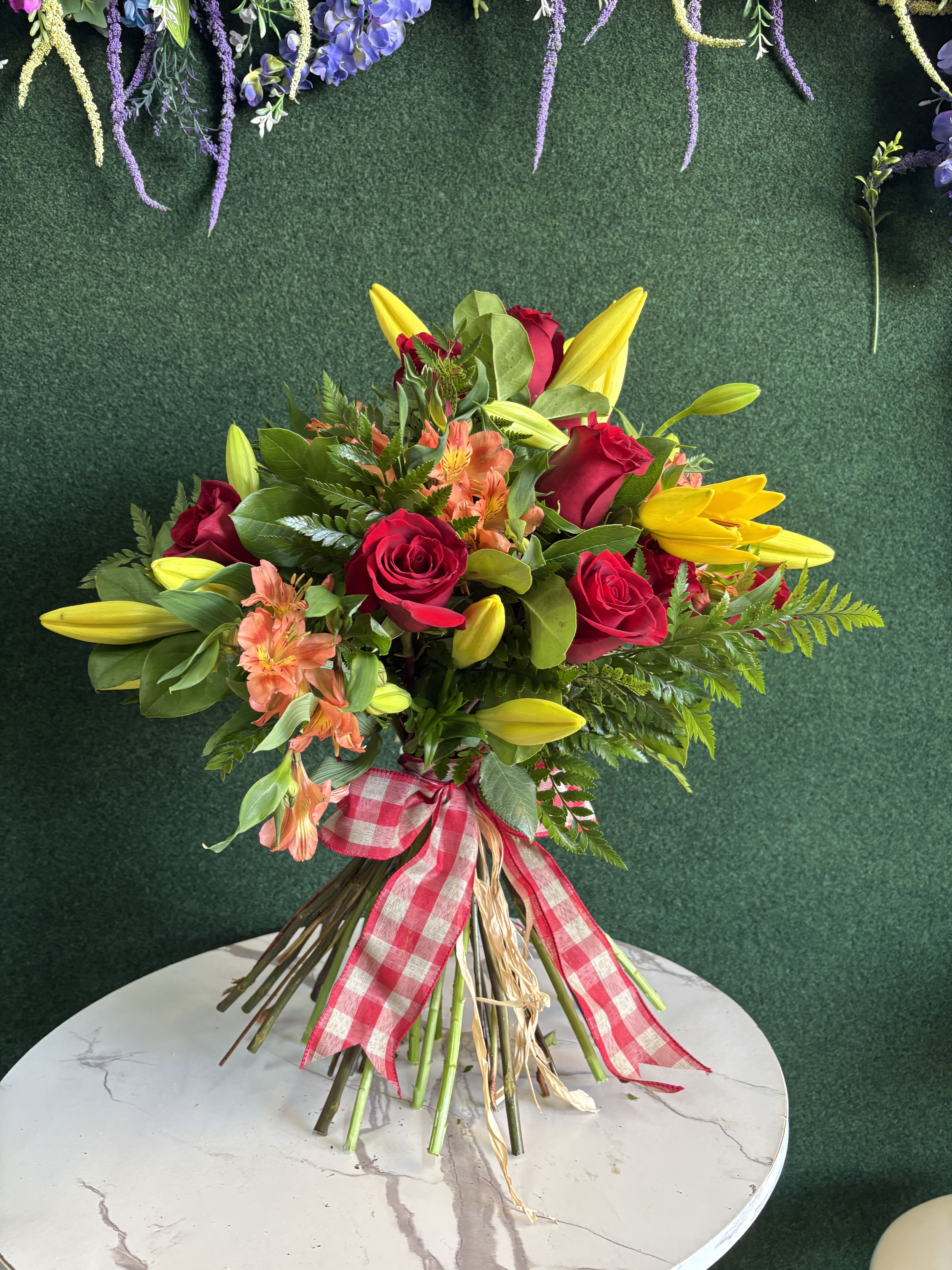 Bouquet of red roses, yellow lilies, and peach flowers tied with a gingham ribbon