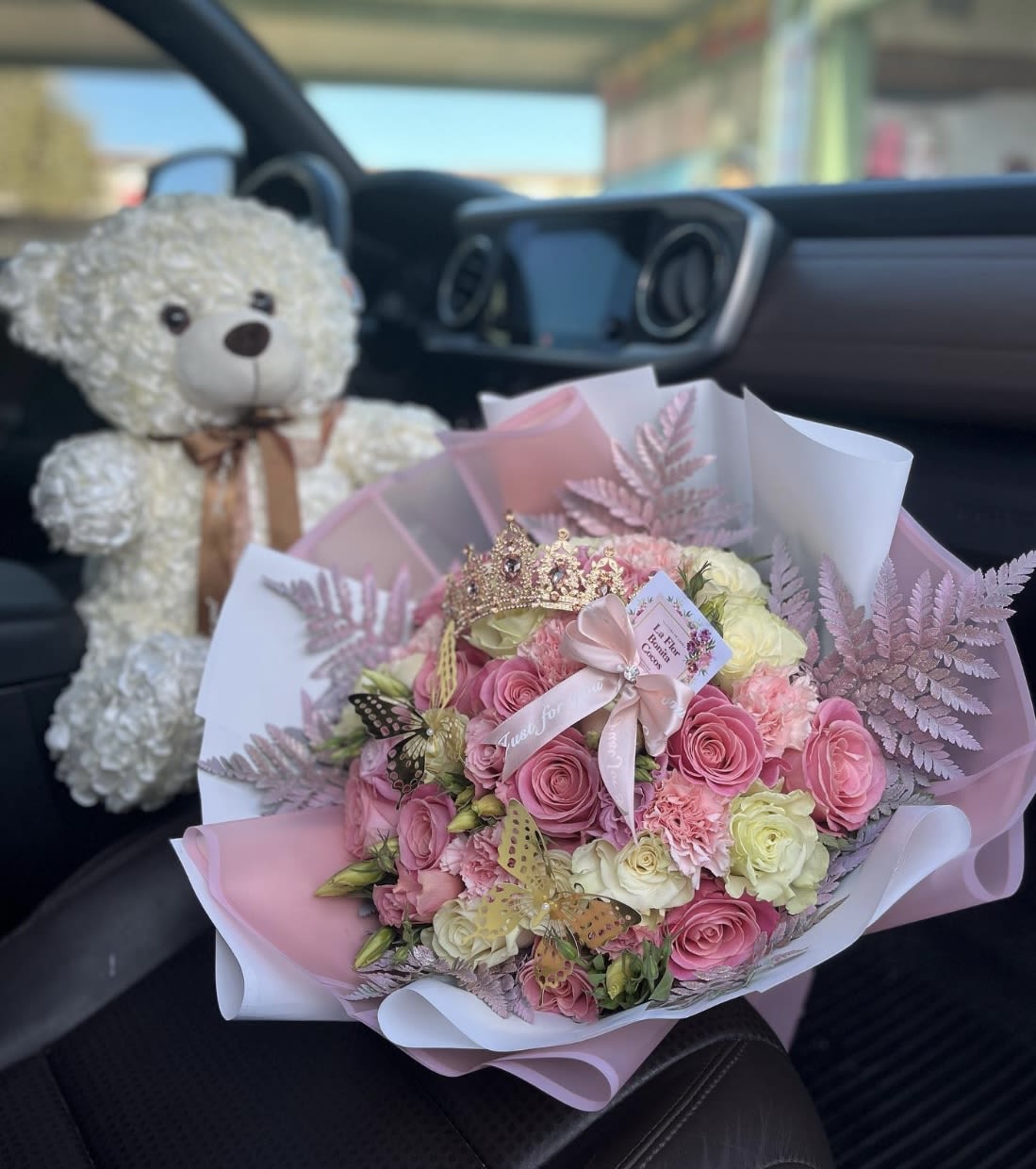 Pink and white rose bouquet with a teddy bear and crown in a car seat