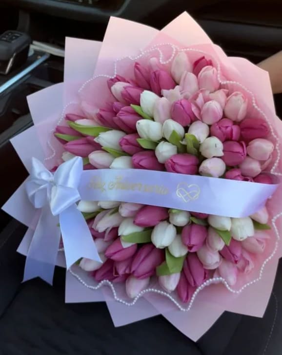 Bouquet of pink and white tulips wrapped in pale pink paper with a white ribbon