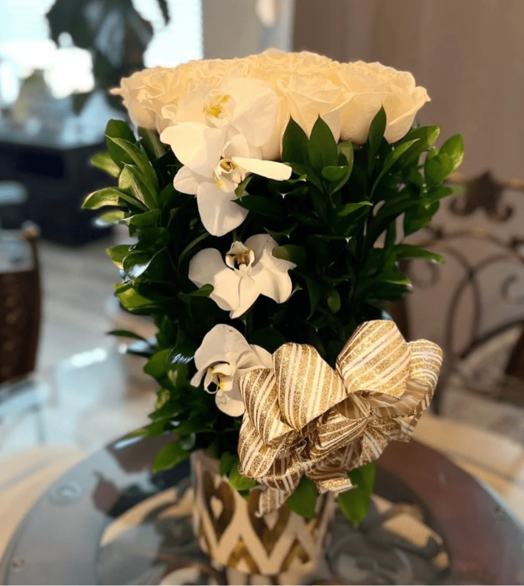 White roses and orchids in a tall arrangement with a striped ribbon bow.