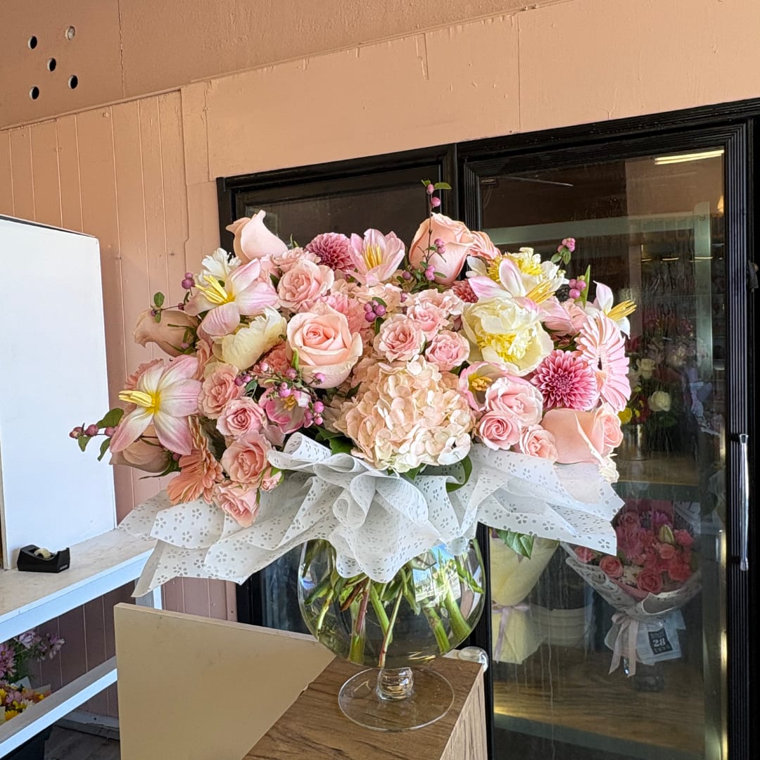 Pink and peach floral arrangement in a glass vase with a white lace wrap.