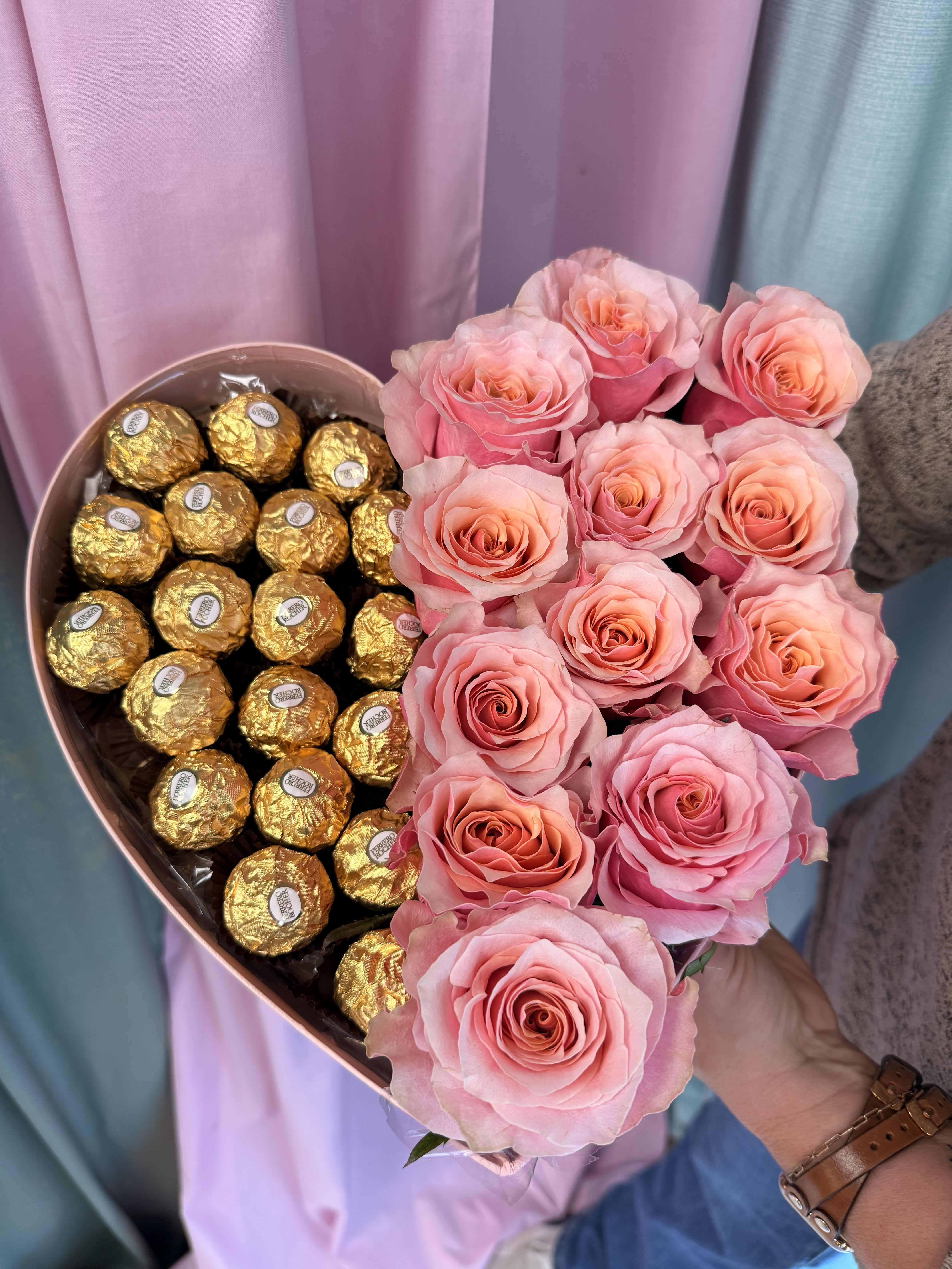 Pink roses arranged beside gold-wrapped chocolates in a heart-shaped box