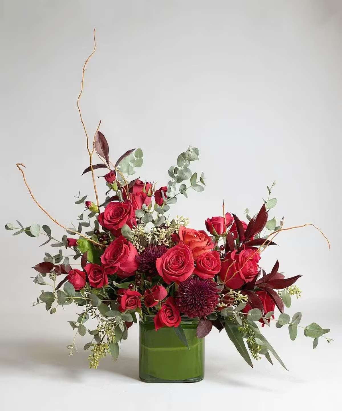 Red roses arranged in a green glass vase with airy foliage