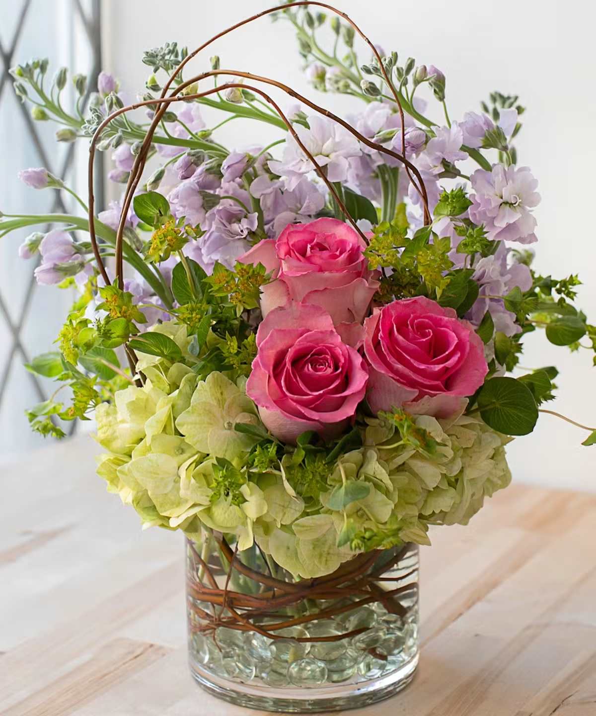 Pink roses and lavender flowers in a glass vase with curly branches