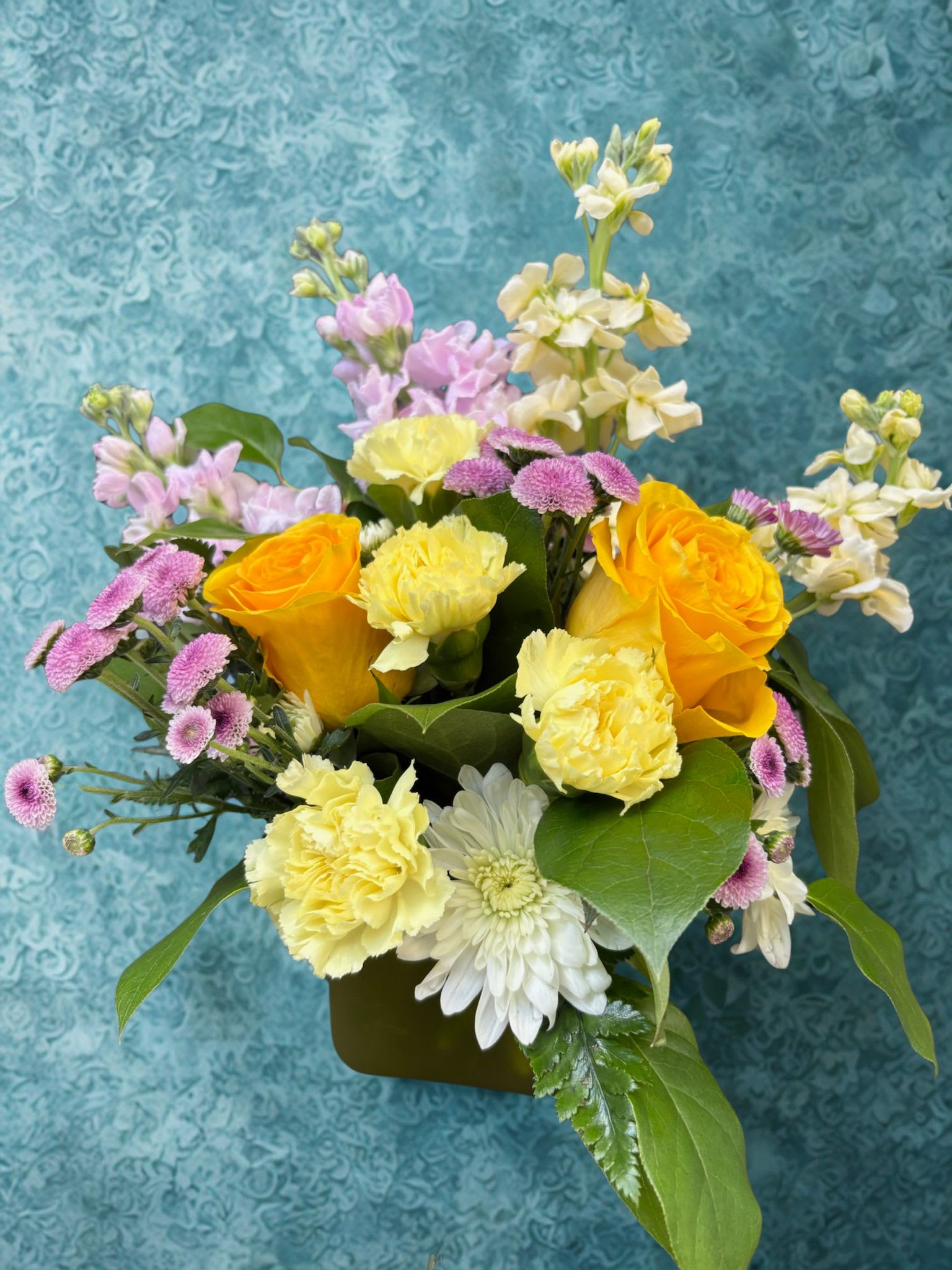 Simply Pastel - Bright yellow roses take center stage in this springlike flower arrangement, making it a cheerful birthday bouquet or a sunny thank-you gift that will brighten someone's day. Soft pink, stock-like blooms rise behind the main cluster to add gentle height and romantic contrast, while white daisies and pale yellow carnations keep the mood light and joyful-perfect for celebrations or to tell someone you're thinking of them.