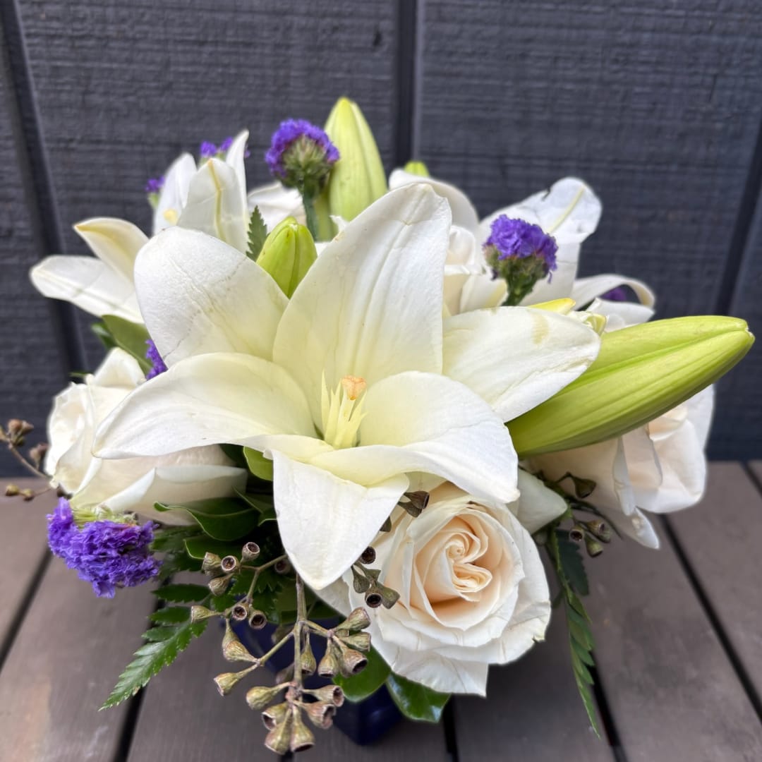 White lilies and cream roses arranged with purple accents in a vase