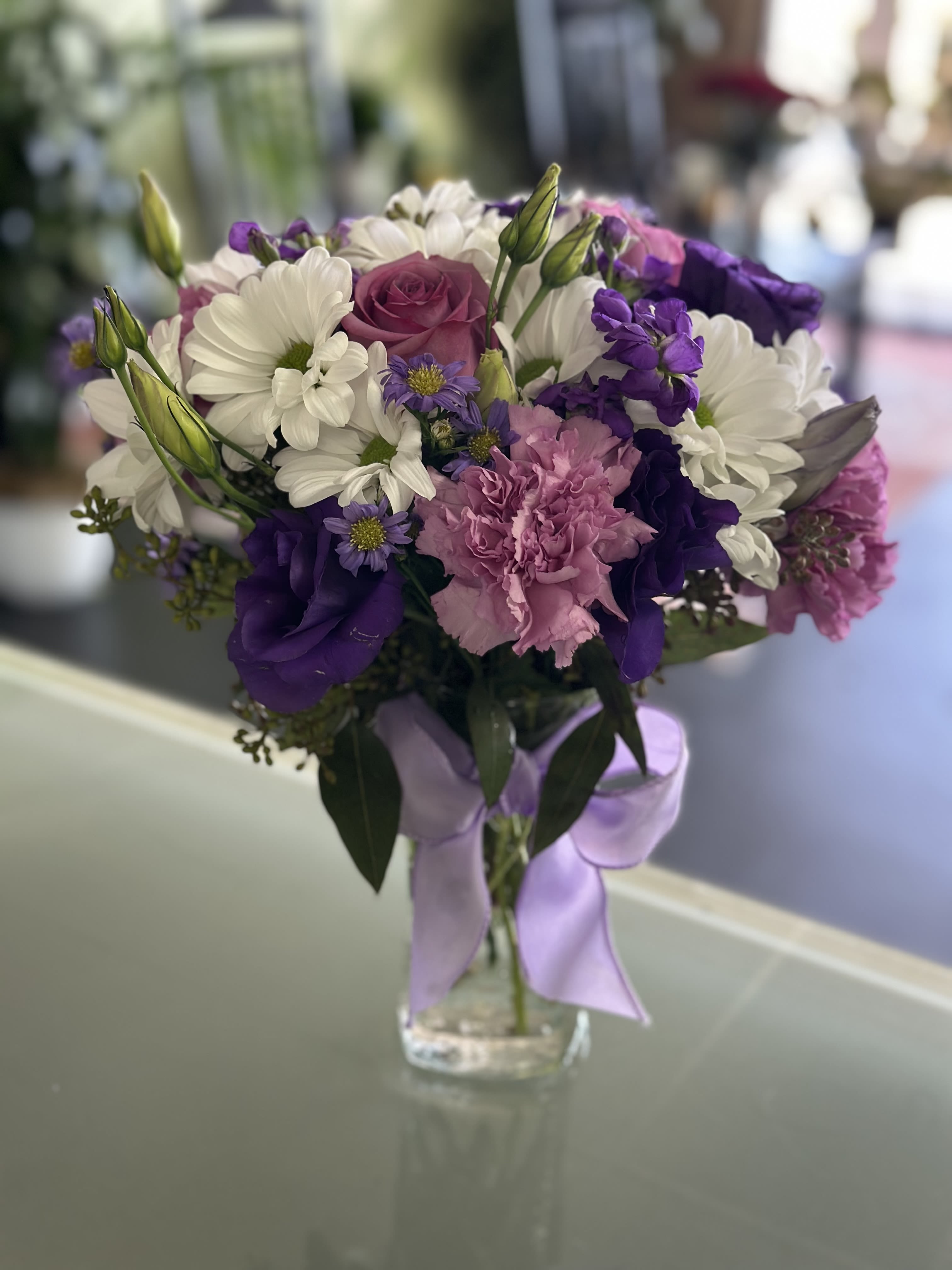 Bouquet of white daisies, purple blooms, and pink carnations in a glass vase