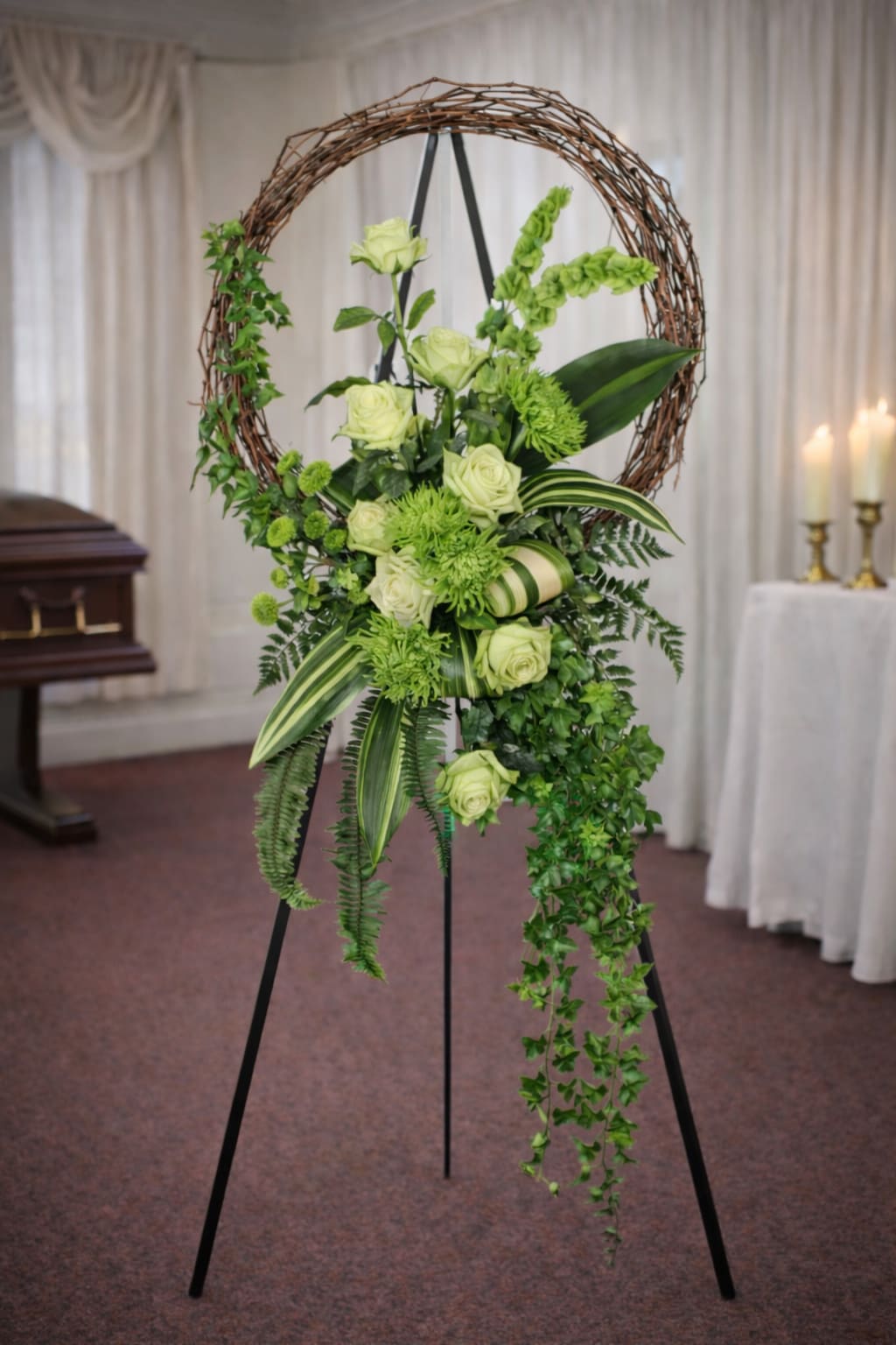 Green floral wreath on a stand with pale roses and trailing greenery