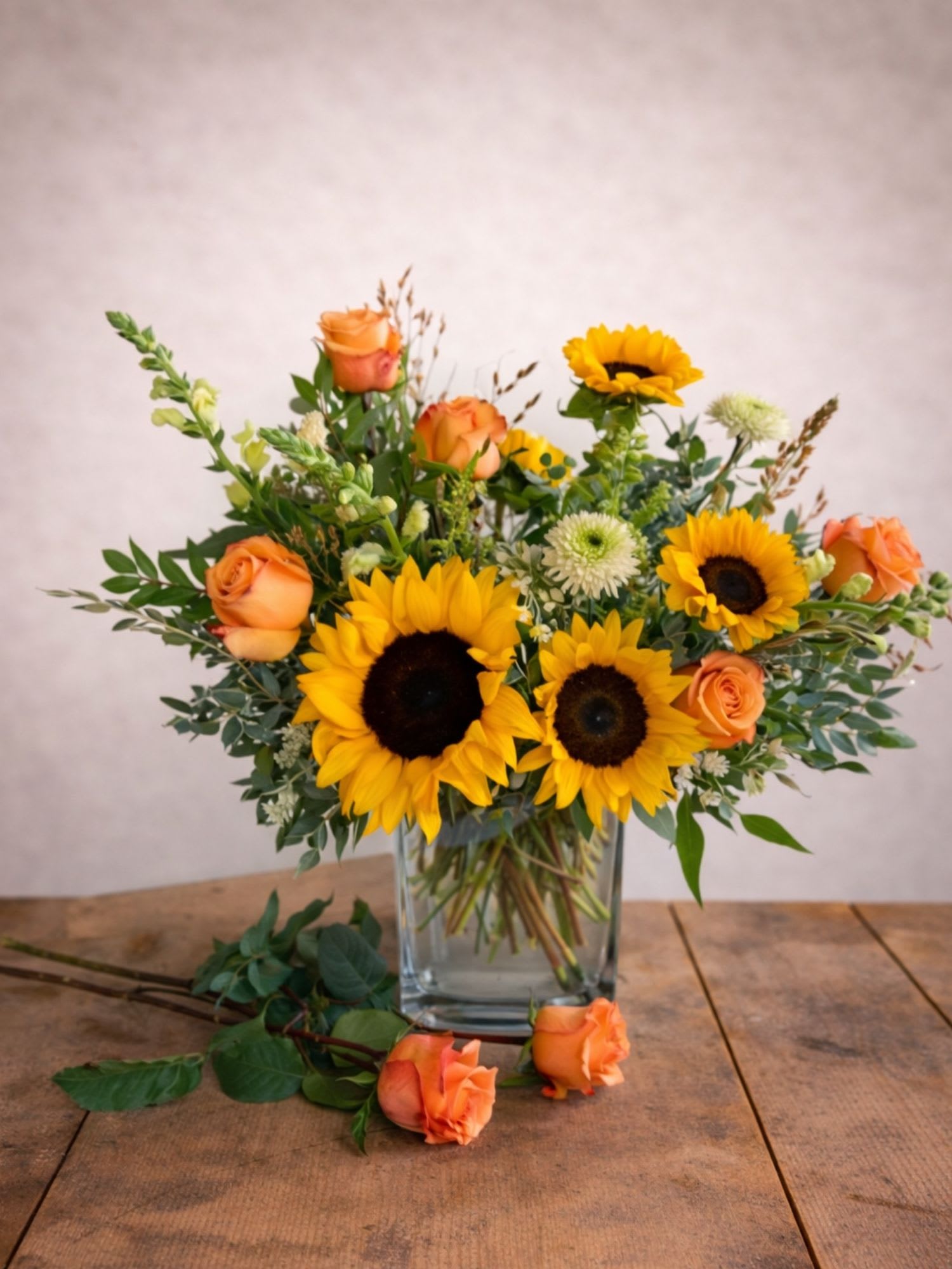 Sunflowers and orange roses arranged in a clear glass vase