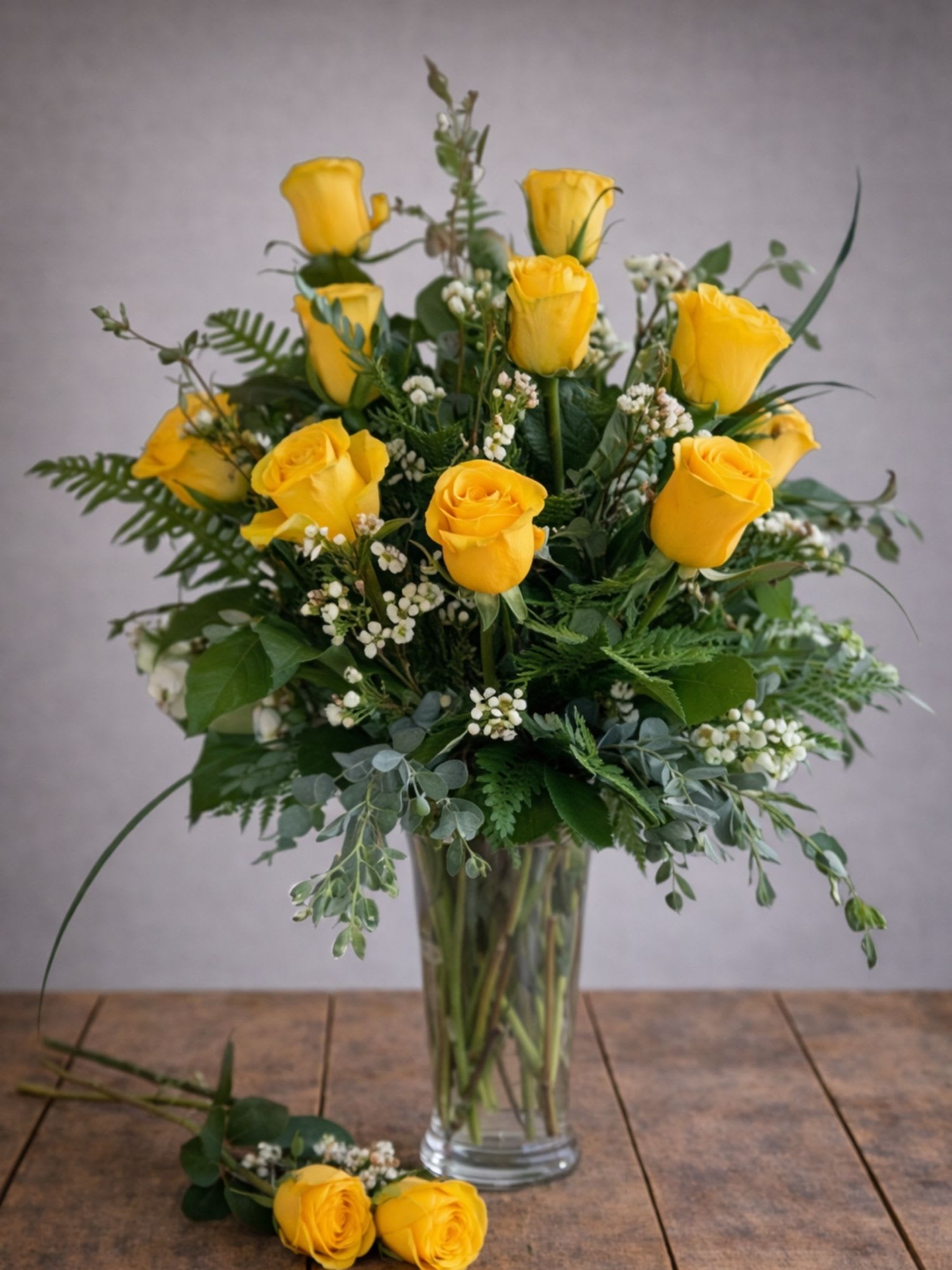 Yellow roses arranged in a clear glass vase with greenery