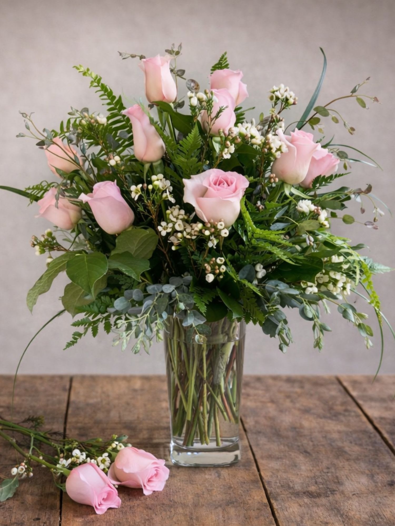 Pink roses arranged in a clear glass vase with mixed greenery.