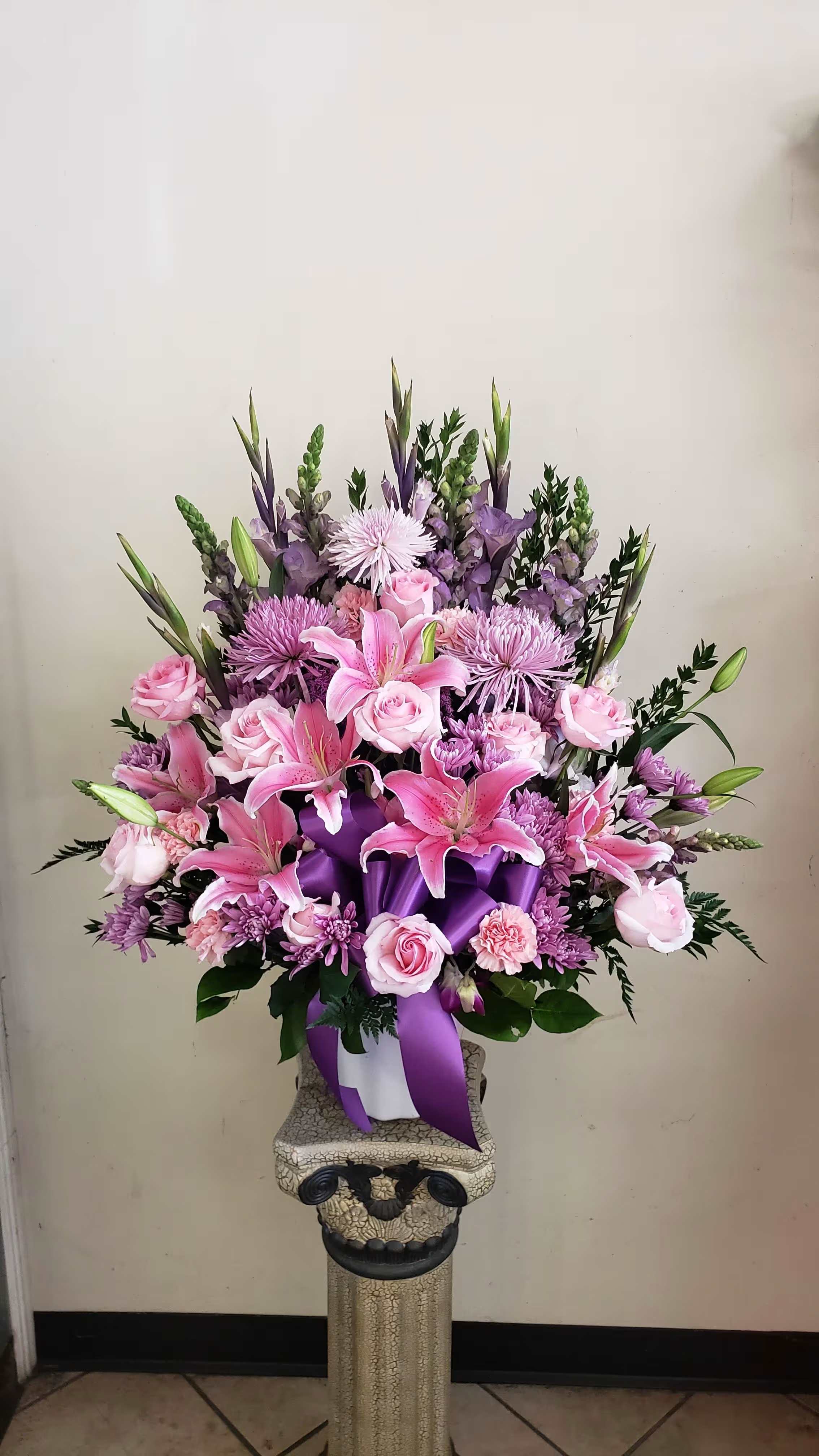 Pink and purple floral arrangement in a white container with a purple ribbon