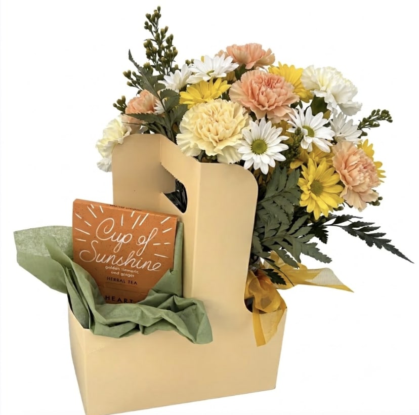 Cup of Sunshine Floral &amp; Tea Gift Caddy - Brighten someone’s day with the ultimate comfort pairing: a vibrant, fresh floral arrangement and a soothing cup of premium tea. Perfectly nestled in a stylish, minimalist gift caddy, this thoughtfully curated set is designed to deliver pure joy straight to their doorstep.  What’s Inside: The Blooms: A cheerful, textured mix of soft carnations and crisp daisies, accented with lush seasonal greenery.  The Brew: A box of "Cup of Sunshine" golden turmeric and ginger herbal tea—perfect for cozy afternoons and wellness boosts.  The Presentation: Arranged in an elegant, easy-to-carry cream caddy with soft green tissue accents and a satin ribbon bow.