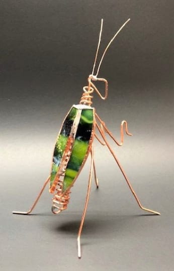 Copper wire insect sculpture with green stained glass body on a dark background