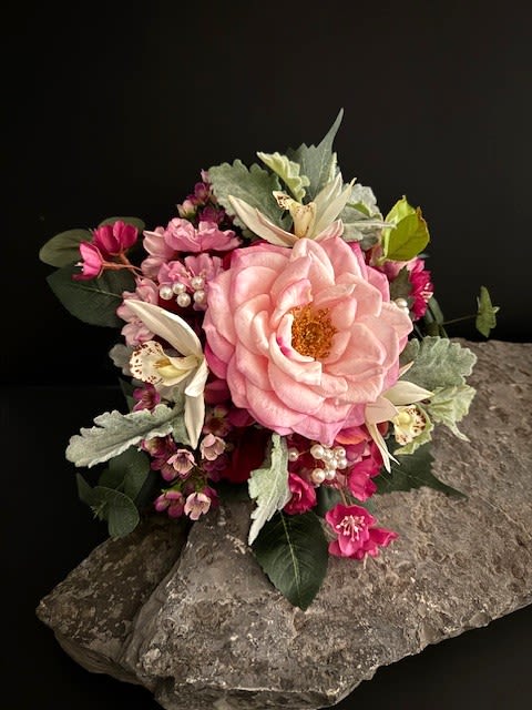 #A029 - Fuschia Hydrangea Silk Floral Bouquet - A lush, hand-held fuchsia hydrangea-style bouquet centered on a single large pink rose creates an immediate romantic statement-perfect as a wedding bouquet or an anniversary gift. The rounded, tightly clustered form mixes vivid pink blooms with white lily-like flowers and pale green foliage for a feminine, sentimental look that will make the person you're thinking of feel truly cherished.  The arrangement includes roses, lilies and mixed seasonal blossoms tucked with rounded green accents and decorative pearl "berries" for a soft, textural contrast. Stems are wrapped in white satin, finished with rows of tiny pearls for a refined, formal touch; the design is shown both gathered for carrying and can be displayed in a clear ribbed glass vase atop a dining room table. Whether you're planning a wedding, marking an anniversary, or sending a heartfelt birthday or Mother's Day surprise, this compact bouquet reads as both elegant and intimate.   Shipping available - select Delivery, then message us to ship.