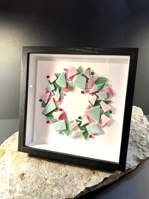 #A088 - Framed Pink &amp; Green Tumbled Glass Wreath - Soft pastel pink and mint-green glass pieces curve into a delicate wreath inside a crisp black shadow box frame - an artful wall piece that reads like framed floral decor. This framed wreath is perfect for Mother's Day, a springtime Easter accent, a housewarming gift, or simply to say "thinking of you"; the gentle palette and jewel-toned beads send a quietly celebratory, thoughtful message to the person you're honoring.   The composition uses triangular and irregular pastel glass and ceramic pieces in pink, green, white and touches of red, arranged on a clean white mat to form a circular, wreath-like design. Small decorative beads and pastel glass accents add subtle sparkle and dimensional texture against the minimalist background; the black shadow box offers a modern gallery look that suits living rooms, nurseries, offices, or hallways. For birthdays, new babies, graduations, or "just because" moments, this framed wreath makes someone feel noticed and cherished without overwhelming their space. Ready to hang or place on a shelf, the piece is an easy-care, year-round decorative gift that keeps the feeling of fresh spring blooms alive long after the season has passed.  Shipping available - select Delivery, then message us to ship.