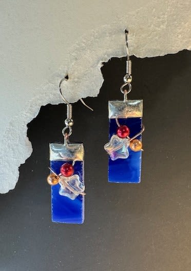 #A120 - Fourth of July Stained Glass Earrings - Deep blue rectangular glass drops catch the light like a slice of summer sky - these dangling earrings are a modern, whimsical gift that reads as both artful and wearable. Perfect as a birthday, anniversary, or Mother's Day surprise (and lovely for Fourth of July or Valentine's Day accents), they send a clear, celebratory message: you're seen and remembered. Each earring features a sleek silver-toned cap and metal ear hook, paired with a clustered mix of beads-a vivid red round bead, a warm golden bead, and an iridescent star-shaped accent that adds subtle shimmer. The clean geometric rectangle contrasts with playful color pops, making them easy to wear with casual daytime looks or as a bright detail beside a floral arrangement.   Give them as a cheerful "thinking of you," "thank you," or "get well" token that brightens someone's day, or tuck them into a gift for weddings, spring and summer celebrations, or just-because moments. Lightweight and eye-catching, they're ready to wear right away and pair beautifully with bold blues or warm-toned bouquets.  Shipping available - select Delivery, then message us to ship.