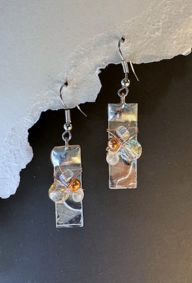 #A086 - Delta Etched Stained Glass Earrings - Delicate etched silver-toned rectangles catch the light with a soft, contemporary gleam-the kind of gift that makes the person you're thinking of feel noticed. These dangle earrings are a dressy-yet-wearable choice for occasions from Mother's Day and birthdays to anniversaries, graduation, or "just because" moments when you want to say thank you or I'm thinking of you. Their narrow silhouette and subtle sparkle also suit holiday parties, prom, or a romantic evening.   Each earring features a narrow rectangular panel finished in a reflective, etched tone and accented near the base with a small cluster of iridescent and frosted beads plus one warm metallic bead, all wrapped in fine wire for an artisanal touch. They hang from simple metal hooks with neatly coiled detailing for a lightweight, comfortable fit-easy to wear all day or save for special events. The mixed white, black, and other muted hues in the beads give a versatile color story that pairs well with spring dresses, autumn layers, or winter coats. Give these earrings as a thoughtful gift for a friend, mom, graduate, or bride seeking understated sparkle; they convey affection and celebration without being over-the-top. They arrive ready to gift and are low-maintenance-wipe gently with a soft cloth to keep the metal and beads bright.  Shipping available - select Delivery, then message us to ship.