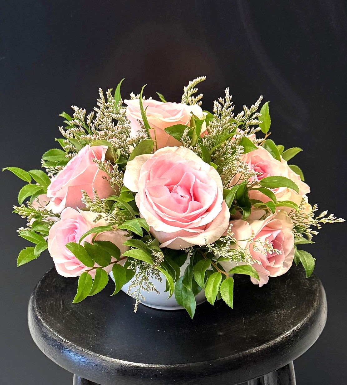 #A095 - Bowl of Sweetness - A compact dome of soft pink roses forms the centerpiece of this low, white ceramic bowl arrangement - perfect as a birthday bouquet, anniversary gift, Mother's Day surprise, or a simple "thinking of you" gesture. The close-packed roses create an immediate impression of tenderness and warmth so the person you're sending it to will feel genuinely celebrated and seen, whether for a housewarming, new baby visit, or just because. Small white filler flowers peek between the blooms, adding delicate texture and bright contrast against the pink and fresh green foliage.   The low, rounded silhouette sits neatly on tabletops or at the center of a Thanksgiving or holiday table without blocking conversation. Sized to fit the included ceramic bowl vase, this arrangement is easy to place and enjoy; no special care is required beyond fresh water and a cool spot to prolong bloom life-an elegant, worry-free gift for get well wishes, sympathy, retirement, or to say thank you.