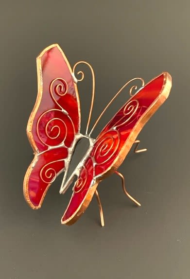 #A043 - Red Resting Butterfly - A bright jewel-toned accent that lifts the room - this small stained-glass butterfly pairs perfectly with a red or orange floral arrangement for birthdays, anniversaries, or to say "thinking of you." The Red Resting Butterfly serves as a cheerful keepsake the recipient can display long after the flowers fade, adding a playful, uplifting touch to bedside tables, desks, or mantels. Crafted in rich red with hints of orange, each wing is composed of smooth stained-glass panels edged in metallic trim and finished with delicate swirling wire details that suggest motion. Thin metal legs and curled antennae give it a sculptural stance so it can stand on a tabletop or shelf; its compact size makes it an ideal add-on gift or decorative complement to a bouquet. This whimsical piece is ready to accompany your floral gift as a lasting reminder of the moment.  Shipping available - select Delivery, then message us to ship.