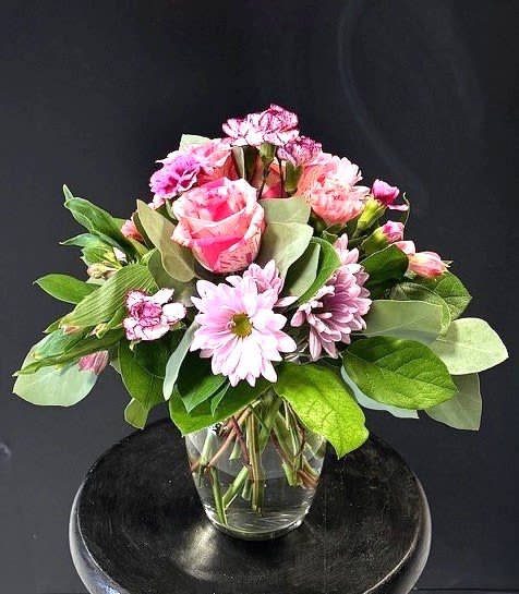 #A045 - Spring Celebration - A bright, affectionate mix of pink roses, magenta-tipped carnations, and soft lavender-pink daisy-style blooms-this flower arrangement is a spring celebration bouquet made for Mother's Day, anniversaries, graduations, or simply to say "thinking of you." The rounded silhouette and pastel palette create a warm, celebratory impression that will make the person you're sending it to feel genuinely seen and cared for. Arranged in a clear glass vase, the stems are visible through the water for a clean, modern presentation that complements the abundant broad green leaves framing the blossoms. The mix includes alstroemeria, carnations, chrysanthemums, roses, and daisies in pinks, purples, whites, and green foliage-a tasteful combination that reads cheerful without being fussy.   Perfect for housewarming, get well, new baby, thank you, or just-because moments, this bouquet is equally lovely for romantic gestures, Mother's or Father's Day, and seasonal spring or summer gifting. Vase dimensions and care: keep water fresh, trim stems every few days, and place away from direct heat to prolong bloom life.