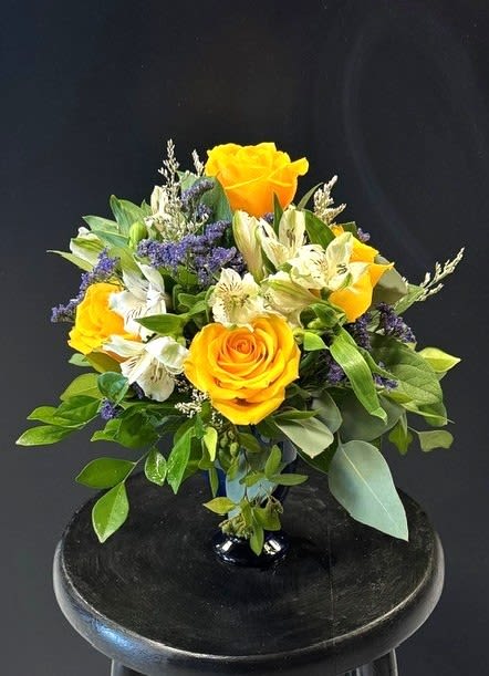 #A060 - Show Your Spirit - Sunny yellow roses, intense purple alstroemeria, yellow daisies, and purple statice brightens this compact, cheerful floral arrangement, perfect for JMU events, birthdays, Mother's Day, Father's Day, or just because. Purple filler blooms add a playful contrast while glossy green foliage frames the rounded bouquet-an uplifting mix that reads as both celebratory and comforting for get well, housewarming, or apology moments. Arranged tightly in a small clear glass vase, the design sits neatly on desks, side tables, or countertops without taking over the room. The palette of yellow, and purple creates a fresh, lively look that works across seasons-spring and summer warmth, autumnal cheer, winter brightness-and suits anniversaries, retirement congratulations, or a simple "thinking of you." Lightweight and easy to place, it's the kind of bouquet that makes the person you're gifting feel genuinely seen and uplifted.