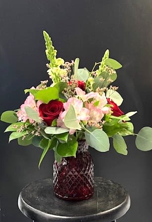 #A100 - Sweetheart Vibes - Velvety red roses clustered with soft pink alstroemeria create an instantly romantic birthday or anniversary bouquet that reads both classic and contemporary. This flower arrangement for Mother's Day and Valentine's Day brings a warm, affectionate message-perfect for saying "I love you," "thank you," or "I'm thinking of you" to the person you care about most.  Compact and rounded at the base, the design is lifted by tall green snapdragon spikes that add elegant vertical movement and a fresh contrast to the rosy center. Arranged in a textured dark red glass vase, the combination of red, pink, and green presents a rich seasonal look that still feels at home for spring, summer, or winter celebrations.  Send this as a thoughtful housewarming, graduation, retirement, get-well, or just-because gift-she or he will feel genuinely seen when these lush blooms arrive. The sturdy glass vase gives the arrangement presence on a mantel or dining table; keep flowers in fresh, cool water and trim stems slightly every few days to extend their life.