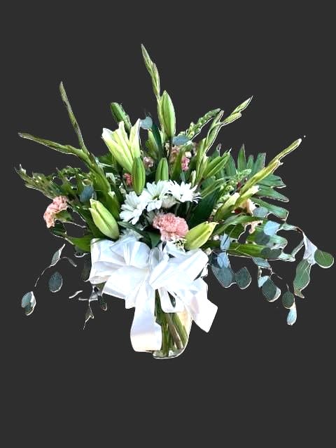 #A068 - Elegant Grace Sympathy Vase - Tall green lily buds reach upward above soft pink carnations and white daisy-style blooms in this sympathy vase, creating a calm, refined impression perfect for a funeral or a thoughtful comfort gift. This flower arrangement for sympathy balances upright structure with gentle color - pink, white, and green to convey quiet support so the person you're thinking of feels comforted and seen.   The bouquet includes alstroemeria, carnations, chrysanthemums, delphinium, daisies, gerbera daisies, hydrangeas, lilies (including asiatic lilies), peonies, roses, snapdragons, stock, and bells of Ireland, arranged with abundant textured foliage for a full, layered look. Delivered in a clear glass vase finished with a white ribbon bow at the neck, the piece presents a formal but understated presence suitable for a memorial service or a bedside tribute. Intended to offer solace, this arrangement is the kind of gift that helps convey sympathy, support, and gentle remembrance. To ensure freshness; water daily and keep away from direct heat for best longevity. 