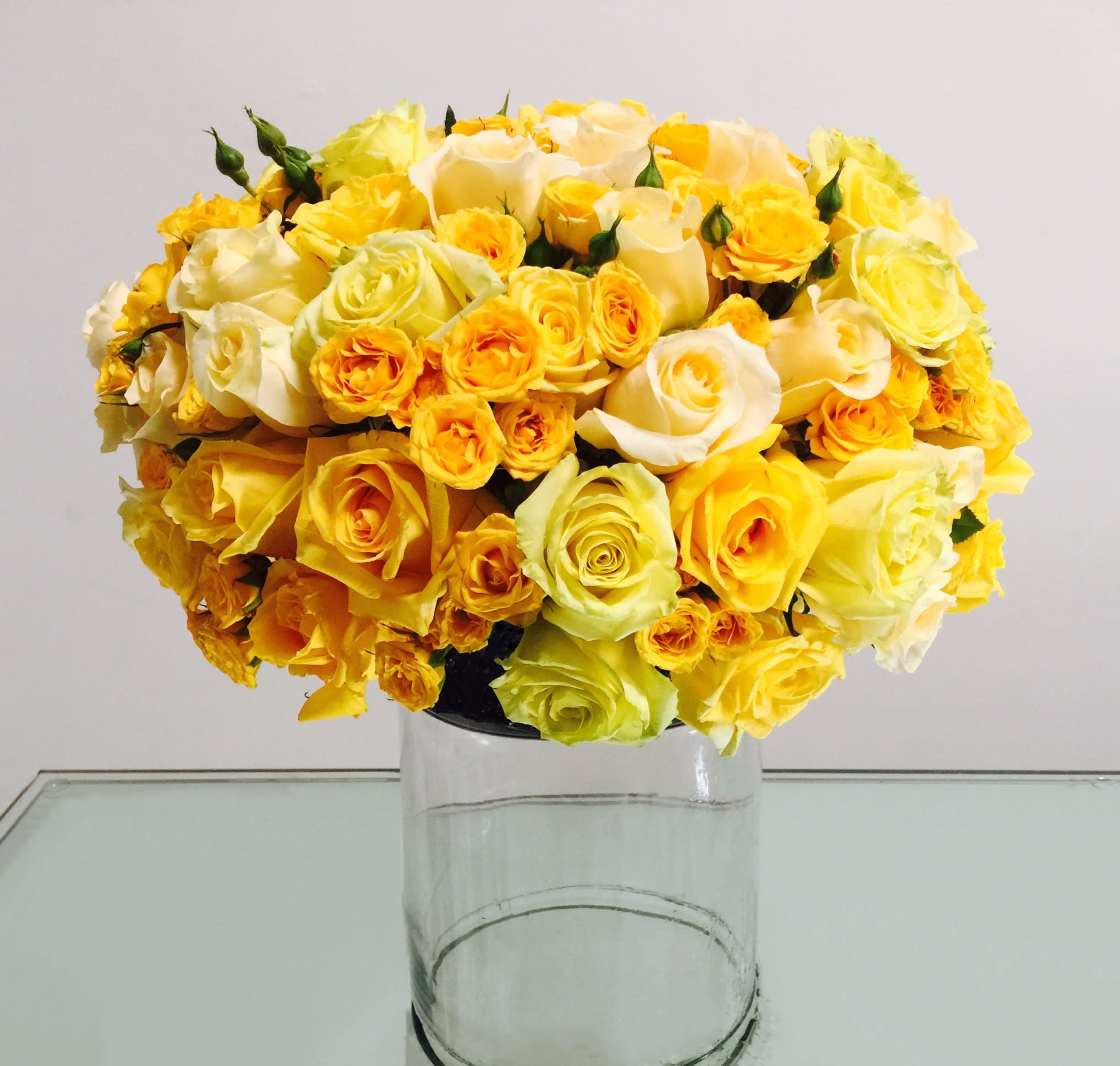 Solar Ray - This bright, golden pavé of Roses and Spray Roses rests atop a clear glass cylinder vase, bringing a glorious ray of sunshine into your home!