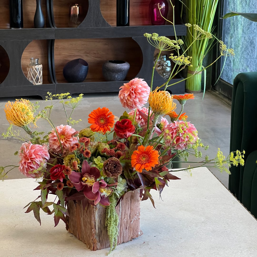 Mixed floral arrangement in a rustic wood container with pink, orange, and burgundy blooms