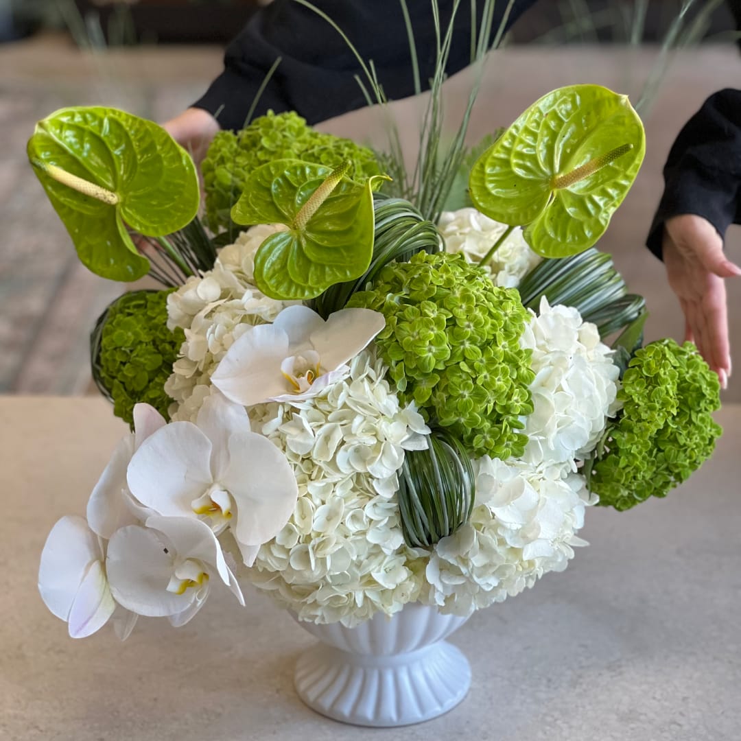 White hydrangea and orchid arrangement in a white vase with bright green anthuriums