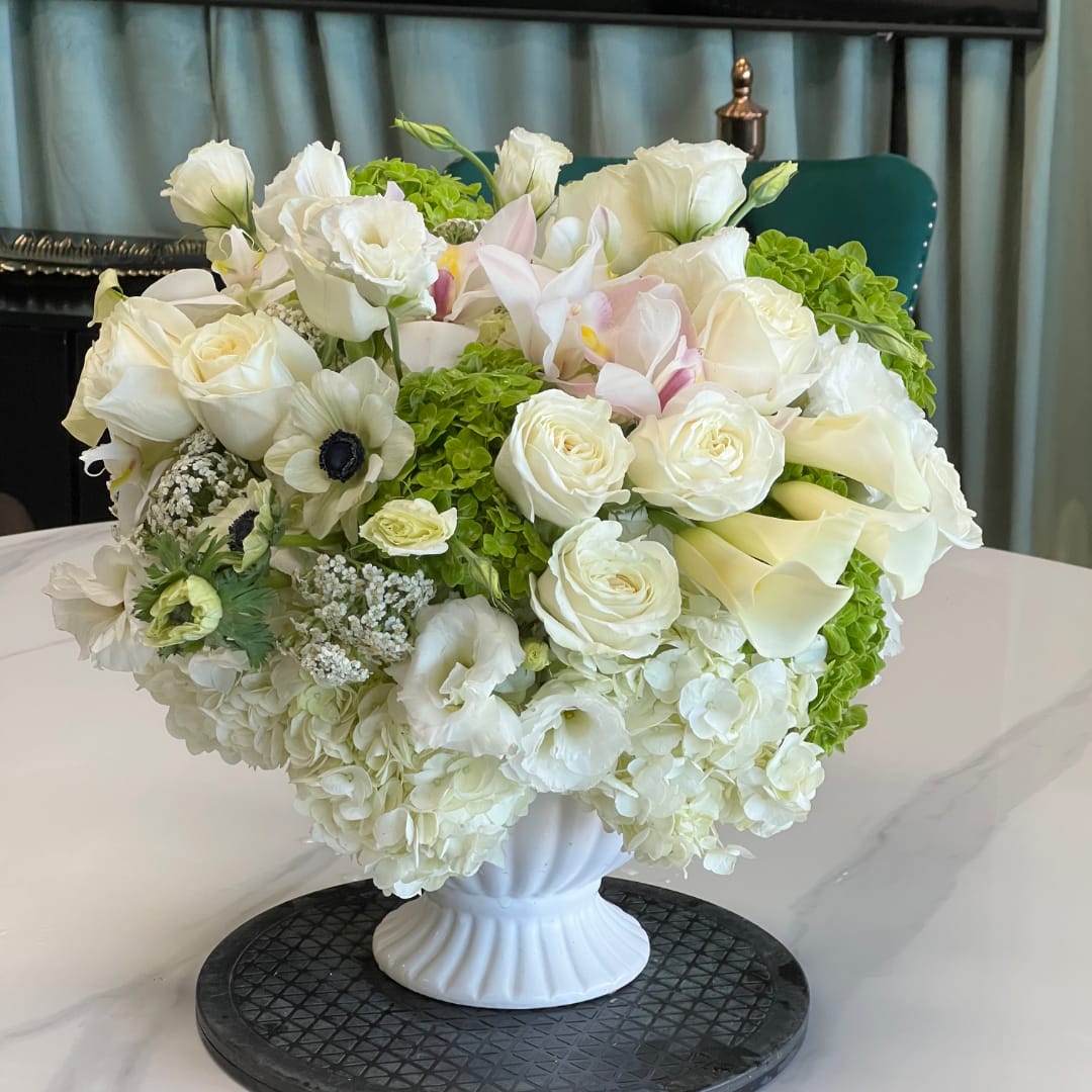 White floral arrangement in a white pedestal vase with green accents