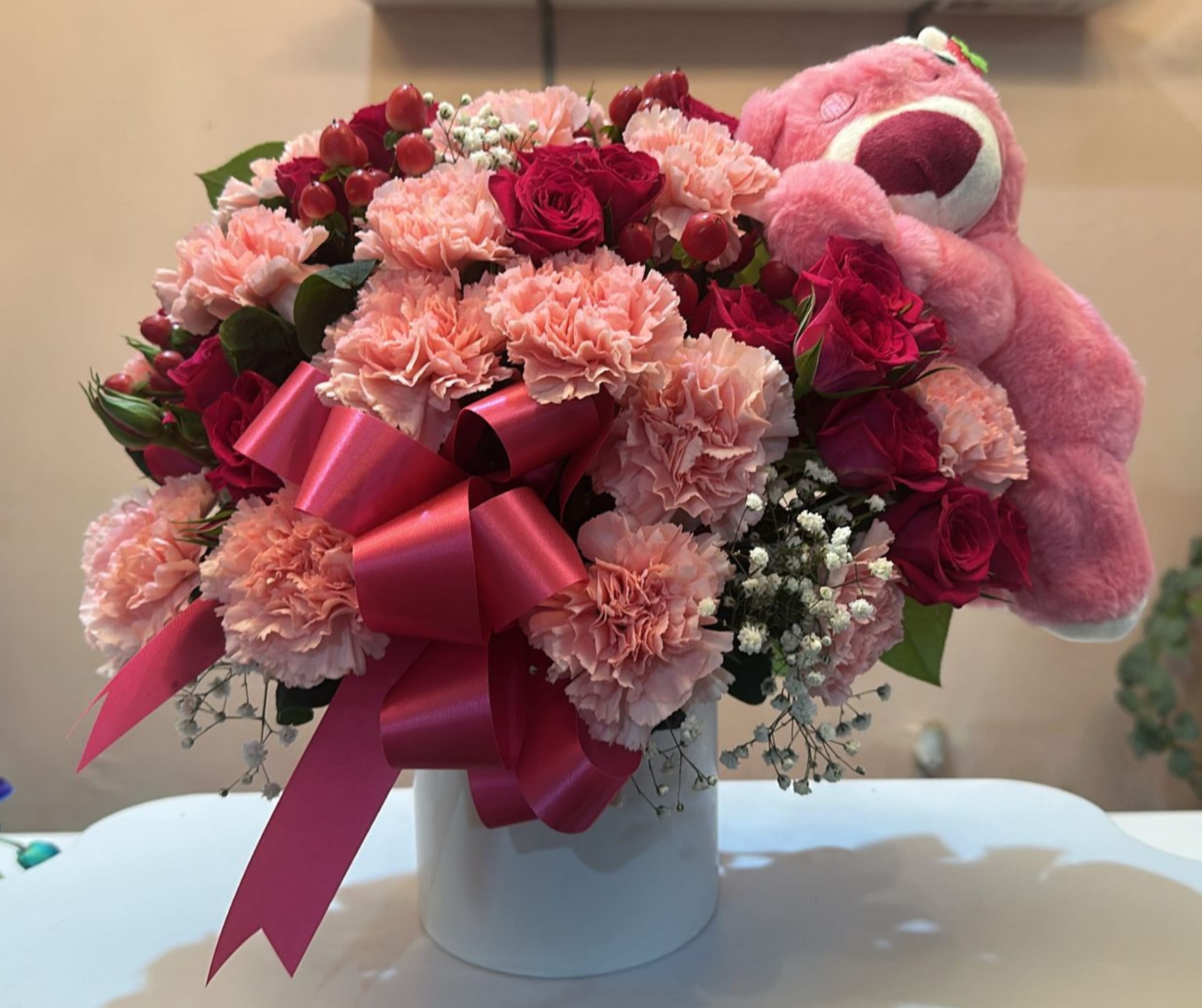 Pink and red bouquet with carnations, roses, and a teddy bear in a white box
