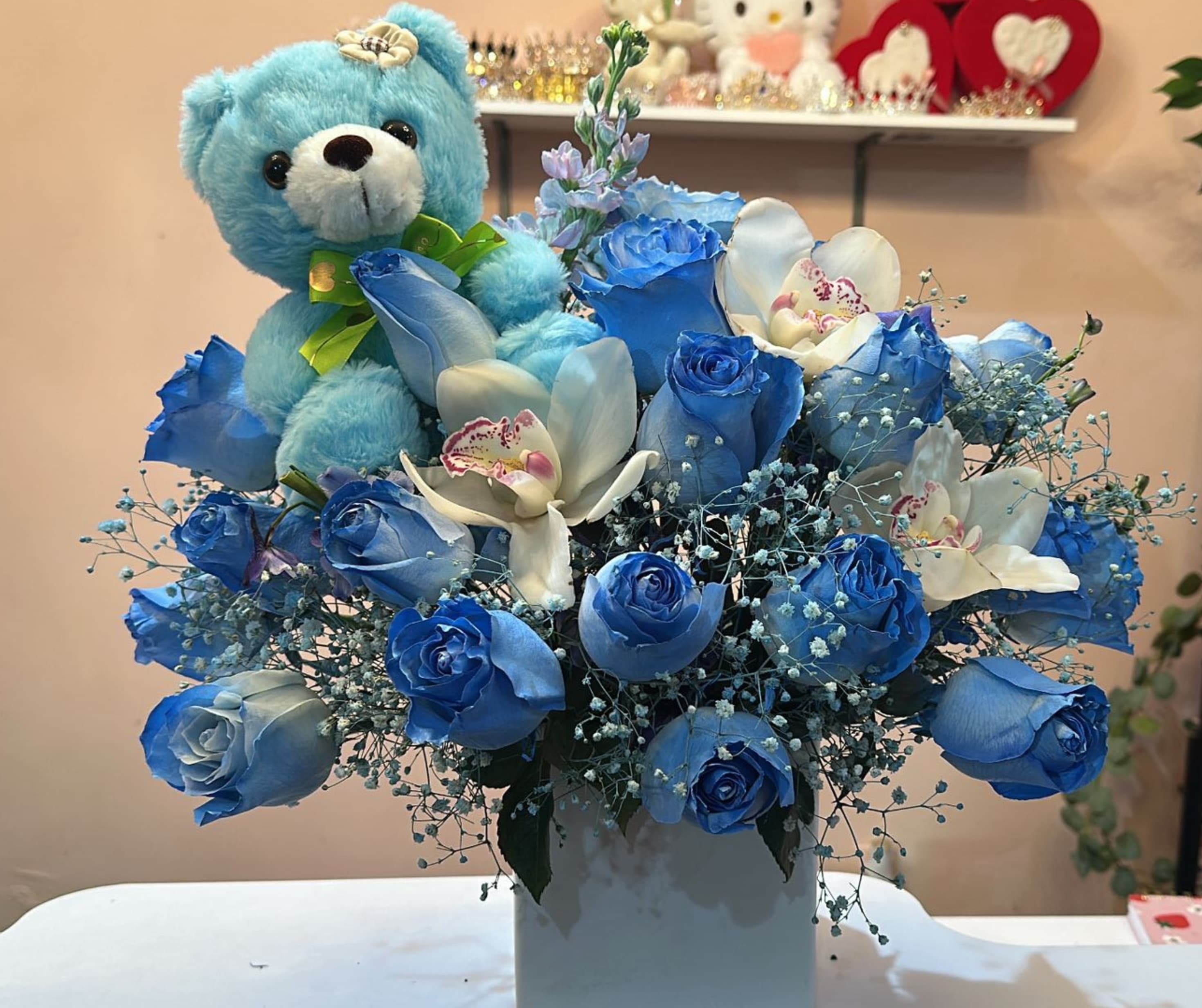 Blue rose bouquet with white orchids and a blue teddy bear in a white vase