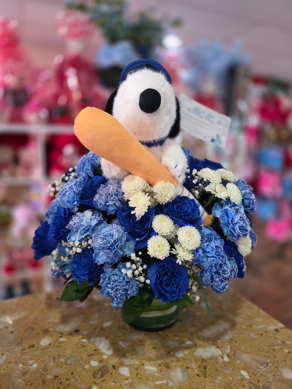 Snoopy plush in a blue flower arrangement holding a toy carrot