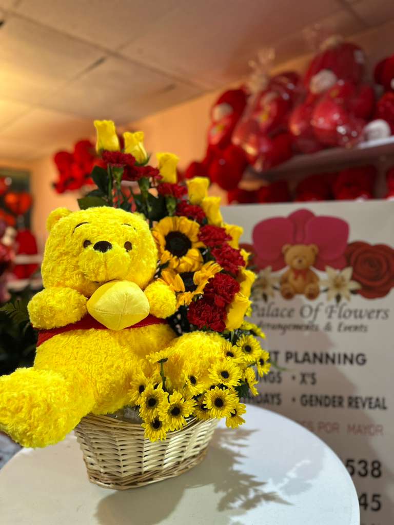 Yellow teddy bear in a wicker basket with red and yellow flowers