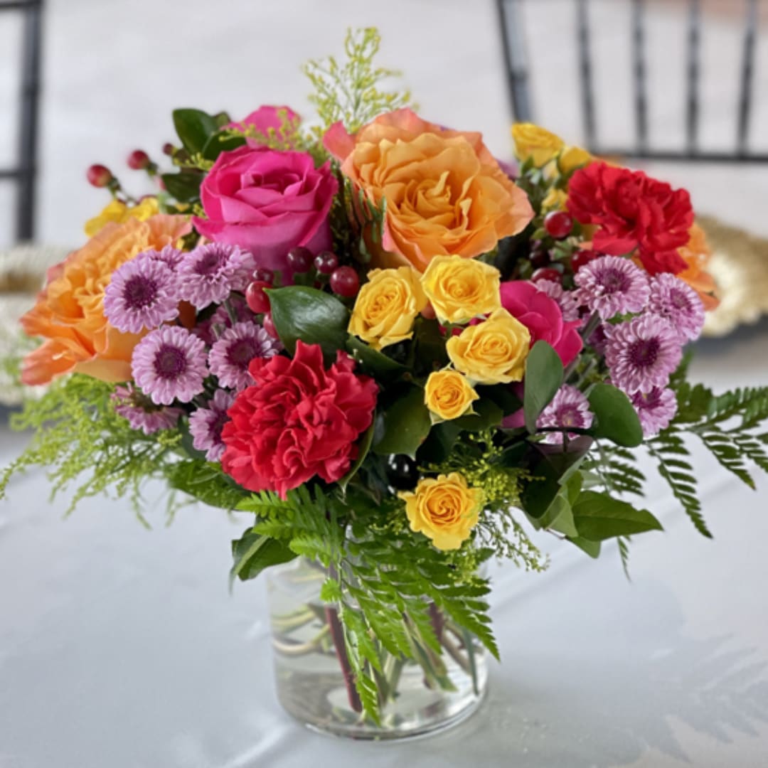 Colorful bouquet of roses, carnations, and daisies in a clear glass vase