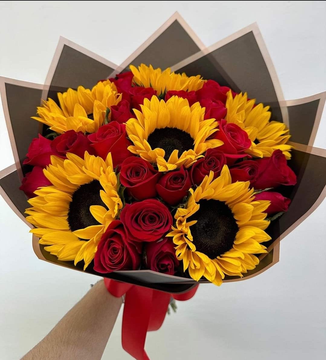Bouquet of red roses and yellow sunflowers wrapped in dark paper