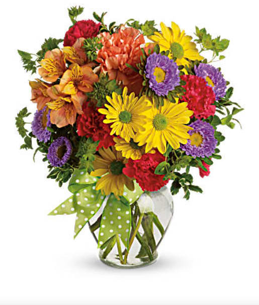 Mixed bouquet of colorful flowers in a clear glass vase with a green polka-dot ribbon