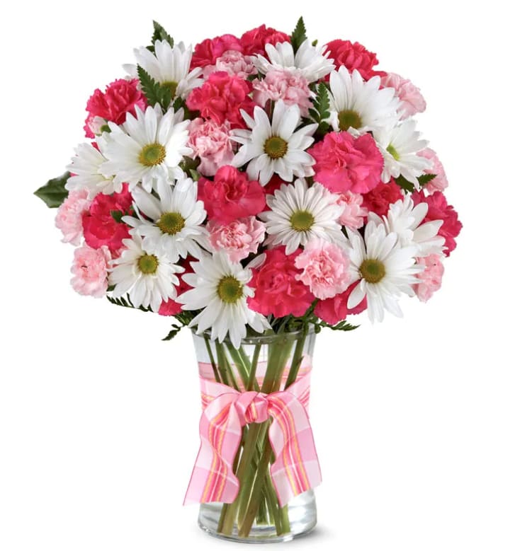 Pink carnations and white daisies in a glass vase with a pink ribbon