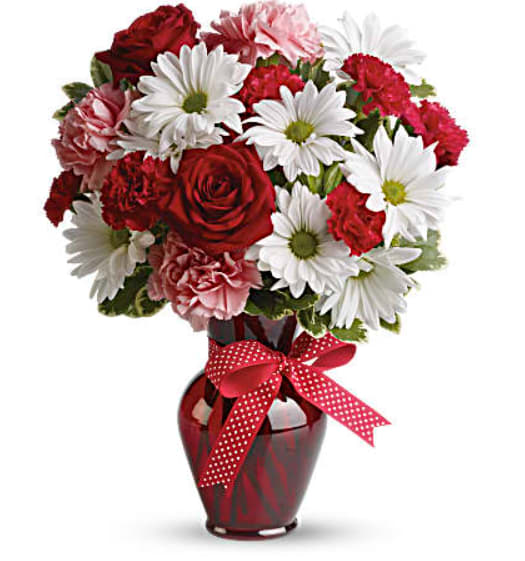 Bouquet of red roses, pink carnations, and white daisies in a red vase with a ribbon