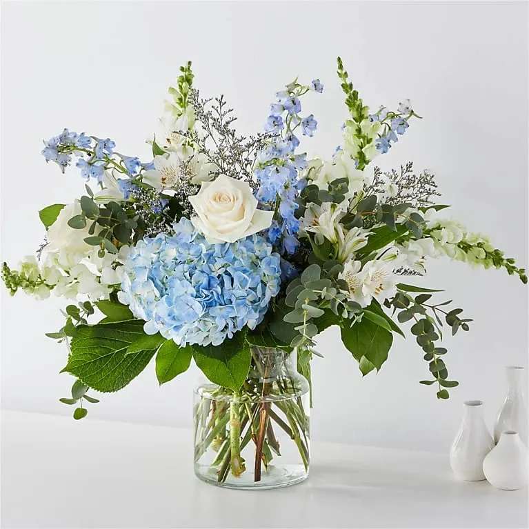 Blue hydrangeas and white roses in a clear glass vase
