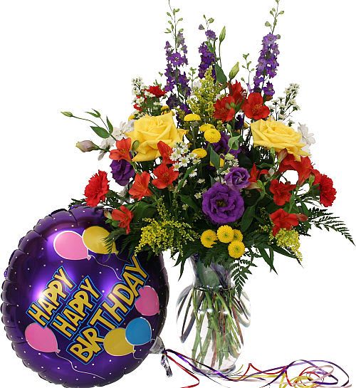 Mixed bouquet in a glass vase beside a purple happy birthday balloon.