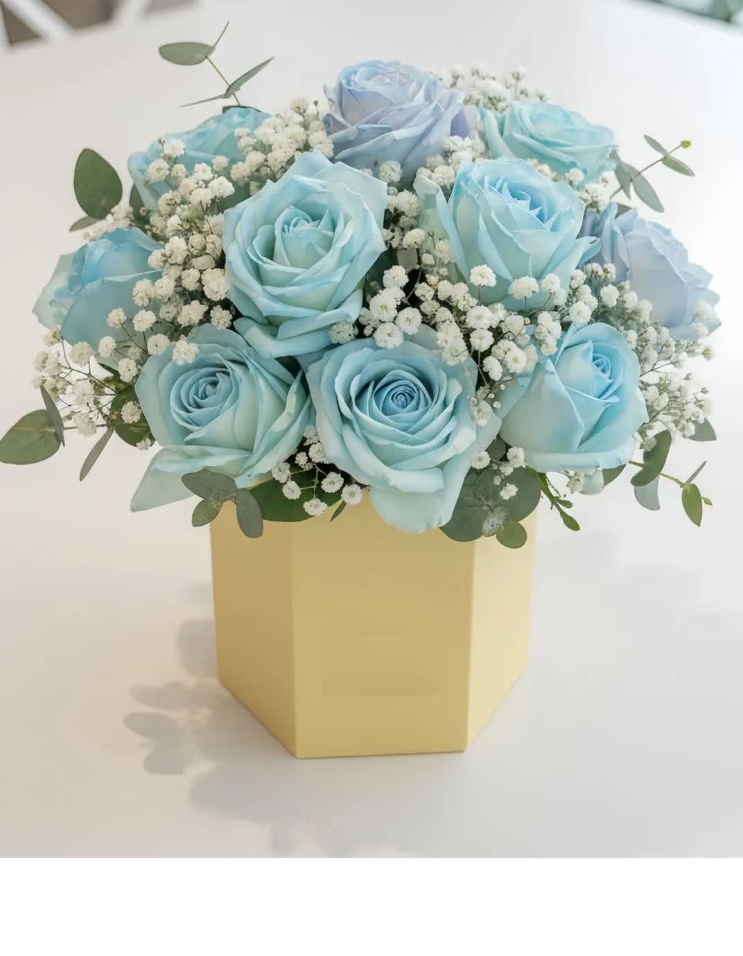 Blue roses arranged in a yellow box with baby's breath