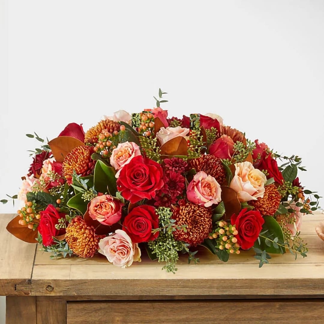 Low arrangement of red and peach roses with orange mums on a wooden table
